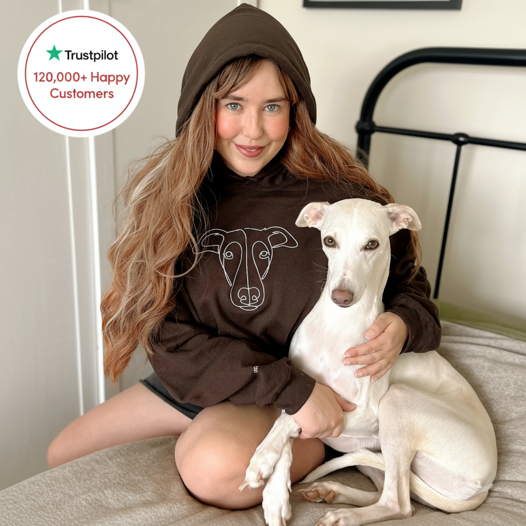 Woman wearing a brown hoodie with a dog design, sitting on a bed with a white dog.